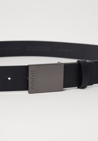 Curea din piele neagră, cu o cataramă din metal negru mat, cu inscripția "HUGO" embosată și o textură netedă, având cinci găuri de ajustare.
