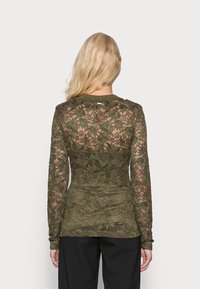 Långärmad spetsblus i olivgrön med blommiga mönster, en figurnära design och ett enfärgat panel vid midjan med rundad halsringning.