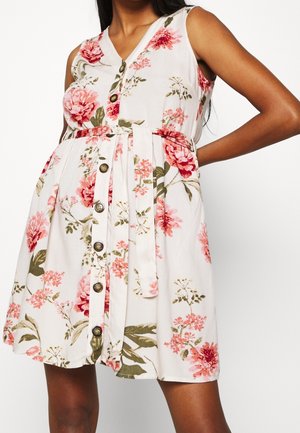 Ærmeløs hvid kjole med pink og grøn blomstret print, knapper foran og matchende stofbælte bundet i taljen.