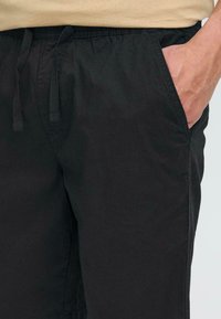 Pantalones cortos ligeros y negros con una cinturilla elástica y cordones, bolsillos laterales y una textura suave y mate.