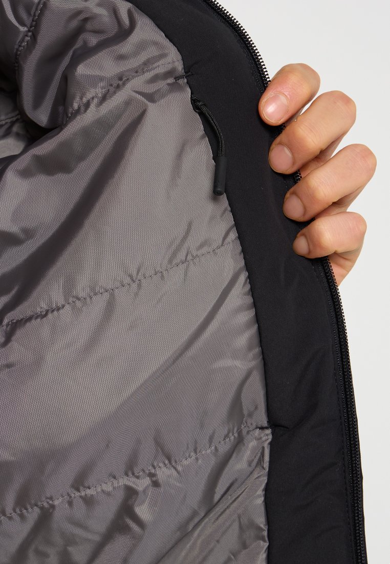 Interno di una giacca a vento nera con un rivestimento grigio liscio. Presenta una cerniera e un piccolo pezzo di elastico per la regolazione sul lato interno.