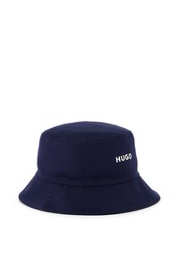 Chapeau seau en coton bleu marine avec un sommet arrondi et un large bord. Présente le logo blanc "HUGO" sur le côté. Texture lisse avec des détails cousus.