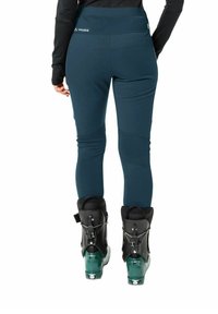 Dunkelblaue Skihosen mit hohem Taillenbund, glatter Textur und tailliertem Schnitt. Schwarze Skischuhe mit grünen Akzenten und verstellbarem Zubehör.