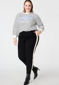 Gestreepte sweatshirt in wit en zwart met de tekst "SUNDAY", gecombineerd met zwarte broek met een crèmekleurige zijstreep. Zwarte laarzen met hak.