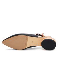 Scarpa con tacco alto in pelle nera con punta affusolata, dotata di un tacco rosa pallido e un fiocco decorativo sulla cinghia alla caviglia. La suola è beige.