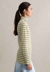 Dopasowany golf w paski w jasnej zieleni i kremowym kolorze, wykonany z miękkiej bawełny. Połączony z dżinsową spódnicą.