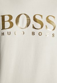 Tissu blanc avec texte doré brillant "BOSS HUGO BOSS" centré dessus.