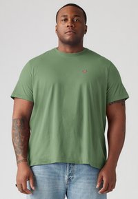 Groene katoenen t-shirt met korte mouwen, ronde hals en een klein rood logo op de borst. Draag het met lichtgewassen denim jeans.