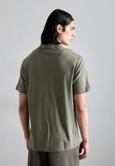Polo shirt vert olive avec un tissu texturé, manches courtes et col classique, vue de dos. Aucun motif ni accent notable.
