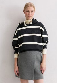 Black and white striped oversized hoodie with embossed "Marc O'Polo," paired with a gray mini skirt. Cotton blend fabric, relaxed fit.