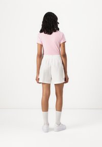 Lys rosa kortermet t-skjorte og hvite shorts med elastisk midjebånd. Modellen har på seg hvite sneakers og ribbestrikkede sokker. Bakview.