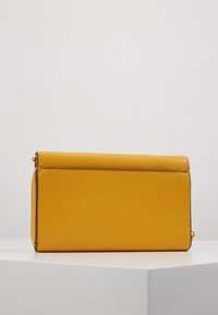 Bolso de mano amarillo de cuero con una textura suave, forma rectangular y cierre de cremallera. Presenta costuras sutiles y un acento metálico.