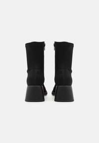 Bottines noires à talon carré, avec un dessus en tissu lisse, dotées d'une fermeture éclair sur le côté. Design minimaliste avec des coutures décoratives.