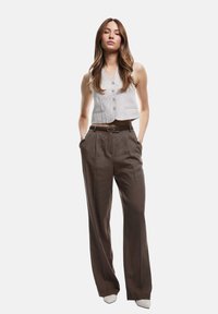 Grijze en witte gestreepte cropped vest met knopen, gecombineerd met high-waisted, wijde bruine broek. Gevoel van textuur, ontspannen pasvorm. Puntige schoenen.