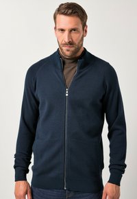 Námořnický svetr na zip s vysokým límcem, texturovaná pletenina, raglánové rukávy a žebrované manžety a lem. Dvě boční kapsy viditelné.