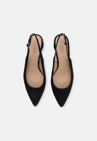 Sorte semskede slingback-hæle med spids tå, åbne sideluftudskæringer og en lille ankelrem. Blødt, glat indvendigt for.