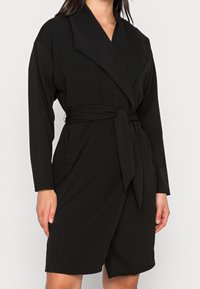 Sort omslagskjole af blødt stof med lange ærmer, dyb V-hals, bred krave og et matchende bindebælte.