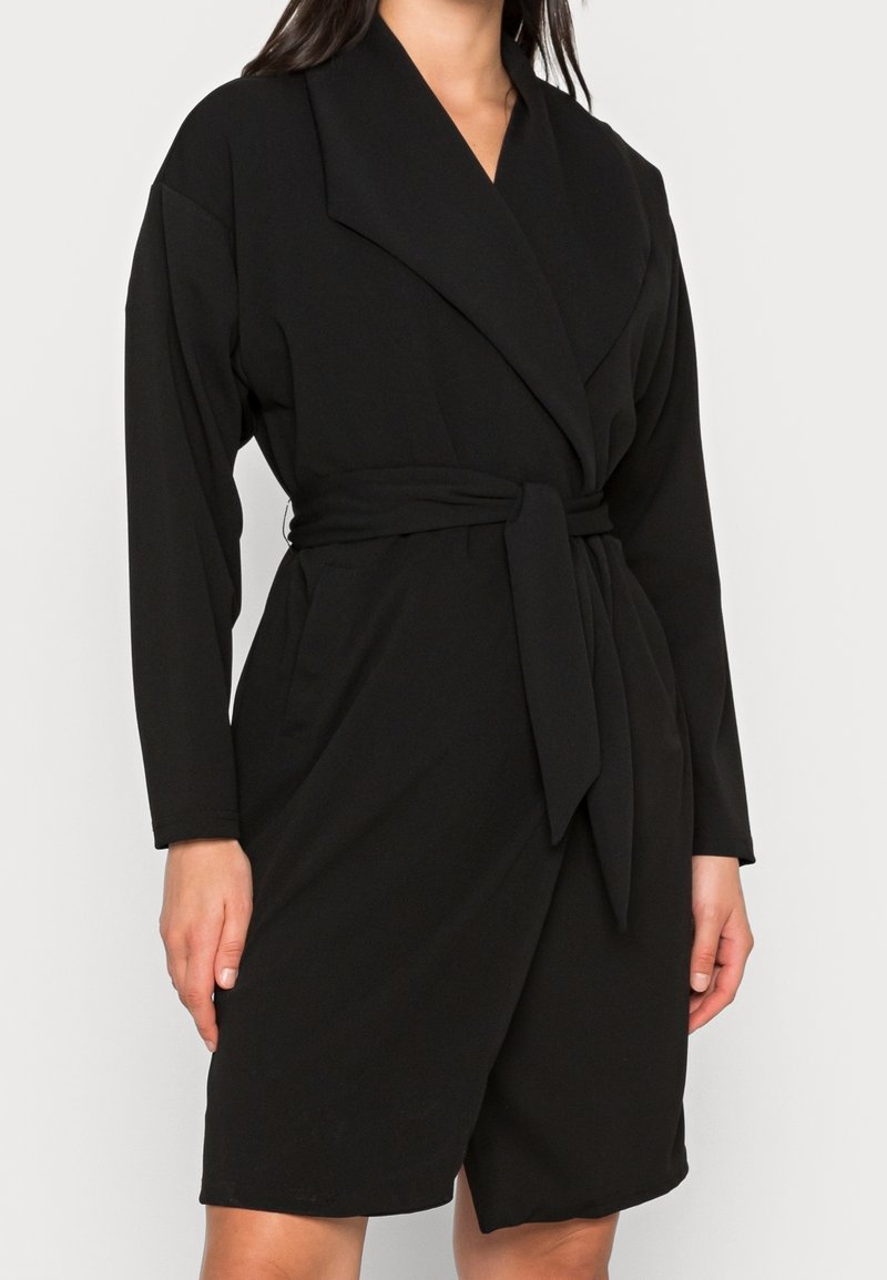 Sort omslagskjole af blødt stof med lange ærmer, dyb V-hals, bred krave og et matchende bindebælte.