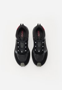 Chaussures de sport noires en mesh et matériaux synthétiques, avec des lacets, un col rembourré, une semelle grise, et des accents rouges et blancs.