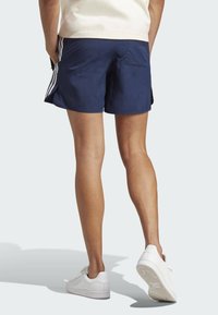 Navy blue athletic shorts with white side stripes, featuring a lightweight fabric and a relaxed fit. Worn with white sneakers.