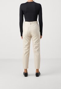 Svart långärmad topp i kombination med beige skräddarsydda byxor, med fickor och smal passform, kompletterat med svarta skor.