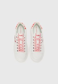 Baskets blanches avec des lacets rouges et des accents de marque. Elles présentent une texture en cuir lisse et un col à motif distinctif.