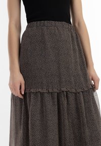Gonna maxi in tessuto nero trasparente con un motivo floreale in beige. Presenta un orlo arricciato e una vita elastica per maggiore comfort.