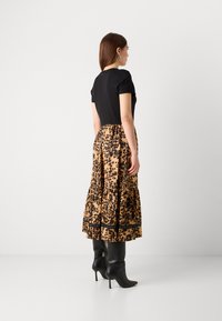 Top nero a maniche corte, gonna midi con stampa leopardata in tonalità beige e nera, design a strati, abbinata a stivali neri con tacco alto fino al ginocchio.