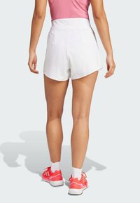 Vita atletiska shorts med hög midja, slätt tyg och böjd nederkant. Bärs med rosa sneakers och vita strumpor.