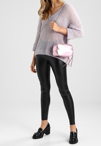 Maglione lavorato a maglia oversize di un leggero viola, leggings neri lucidi, mocassini neri con plateau e una piccola borsa a tracolla metallica rosa.
