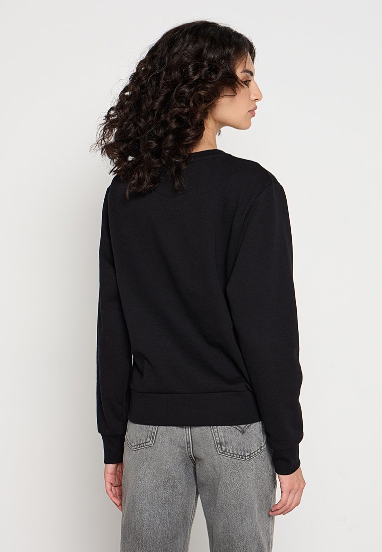 Sudadera negra de manga larga, con cuello redondo y dobladillo acanalado. Combinada con jeans grises. Presenta una textura suave y un diseño minimalista.