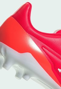 Botín de fútbol rojo brillante en cuero suave con una suela de goma blanca. Presenta un panel texturizado y un diseño de talón reforzado.