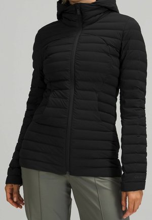 Czarna pikowana kurtka na zamek z wysokim kołnierzem, noszona przez osobę w szarych spodniach, widoczna od ramion do bioder.