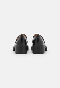 Black patent leather shoes with a low block heel, featuring a sleek rounded back and smooth texture. No visible hardware or accents.