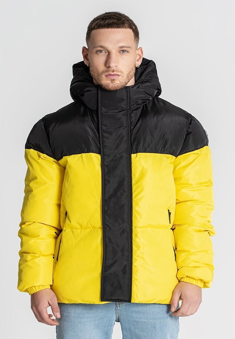 Padded jacket o jas黄色ym korpusie i czarnych ramionach. Posiada wysoki kołnierz, kieszenie na zamek błyskawiczny i elastyczne mankiety.