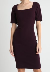 Tight passande knälång klänning i djupt vinröd med korta ärmar och fyrkantig halsringning. Tillverkad av stretchmaterial med en mjuk textur.