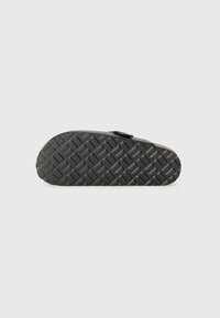 Semelle de chaussure en caoutchouc noir avec un motif de grip texturé ; forme arrondie avec une légère courbure au niveau du talon et un design en couches au niveau de la semelle intermédiaire.