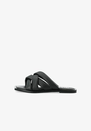 Sandale en cuir noir à glissière avec des brides croisées, semelle plate et design minimaliste. Texture lisse avec un éclat subtile.