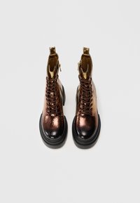 Bottes à lacets pour la cheville avec une finition en bronze métallique et noir, dessus texturé, et une semelle noire épaisse ; elles possèdent une fermeture éclair sur le côté.