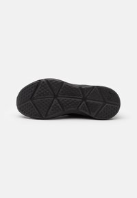 Semelle de chaussure de sport noire avec une surface en caoutchouc texturée ornée de motifs géométriques pour une meilleure adhérence. Sa forme est arrondie avec un design épais.
