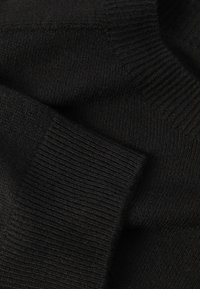 Tissu noir tricoté avec un motif côtelé texturé. Texture lisse avec des épaisseurs variables. Matériau doux et flexible.