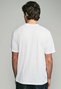 Witte katoenen t-shirt met korte mouwen, ronde halslijn, zachte textuur en zonder patronen of graphics, gezien van achteren.