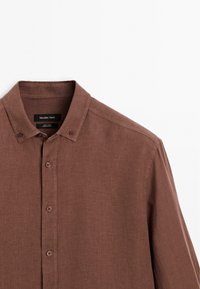 Chemise en lin marron à manches longues avec col boutonné et quatre boutons visibles sur le devant, étiquette Massimo Dutti.