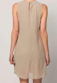 Beżowa sukienka bez rękawów z okrągłym dekoltem, subtelnym zapięciem na guziki z tyłu oraz lekkim, zwiewnym materiałem, sięgająca do połowy uda.