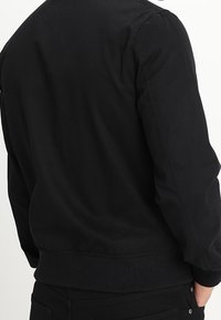 Černá bomber bunda, směs bavlny, přiléhavé manžety a pas, hladká textura, jednoduchý design, žádné viditelné logo nebo vzory na zádech.
