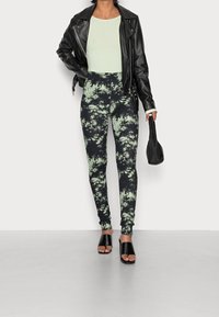 Svart läderjacka över en ljusgrön topp, tillsammans med högmidjade, batikfärgade leggings i svart och grönt, samt svarta sandaler med öppen tå.