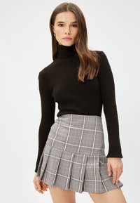Sort ribbet turtleneck sweater parret med en grå ternet mini nederdel med folder, dekoreret med røde og hvide striber.