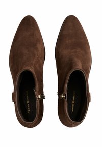 Stivali alla caviglia in suede marrone con punta affilata, zip laterale e finitura testurizzata. Presentano dettagli in metallo color oro e una suola nera.
