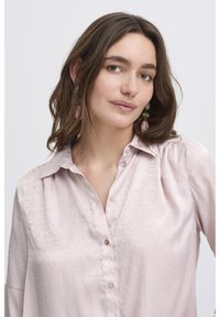Light pink button-up shirt with a soft texture, featuring subtle decorative beading and a classic collar. Long sleeves.