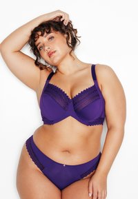 Ensemble de lingerie violet comprenant un soutien-gorge avec des détails en dentelle et une culotte assortie. Le soutien-gorge est à armatures, avec des bretelles réglables et des bords festonnés.